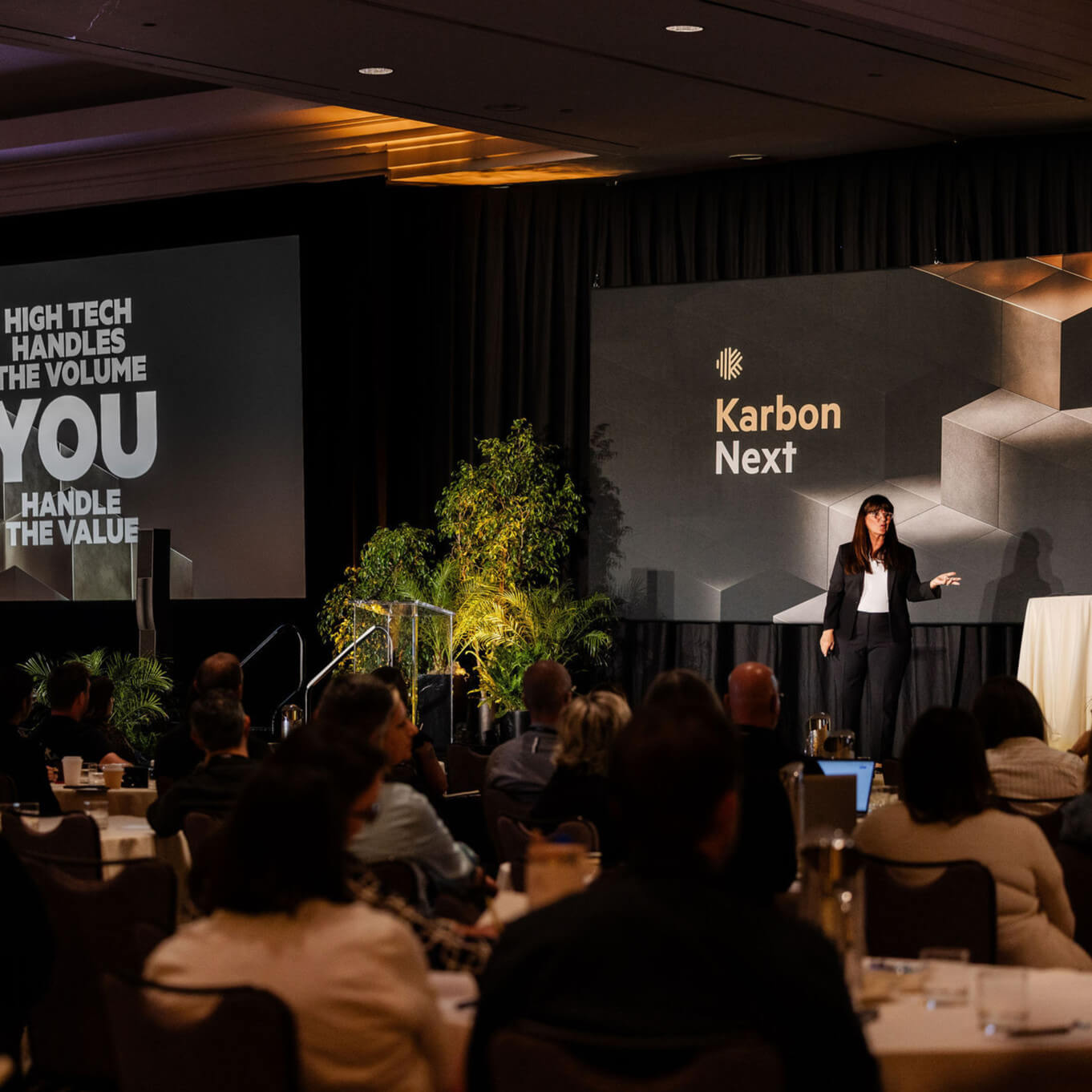 Karbon CEO Mary Delaney presents on stage at a Karbon Next keynote session to a seated audience in a conference room