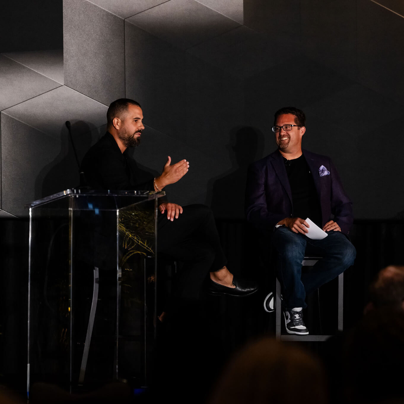 Two speakers on a darkened stage at a Karbon Next session, one at a podium and one seated