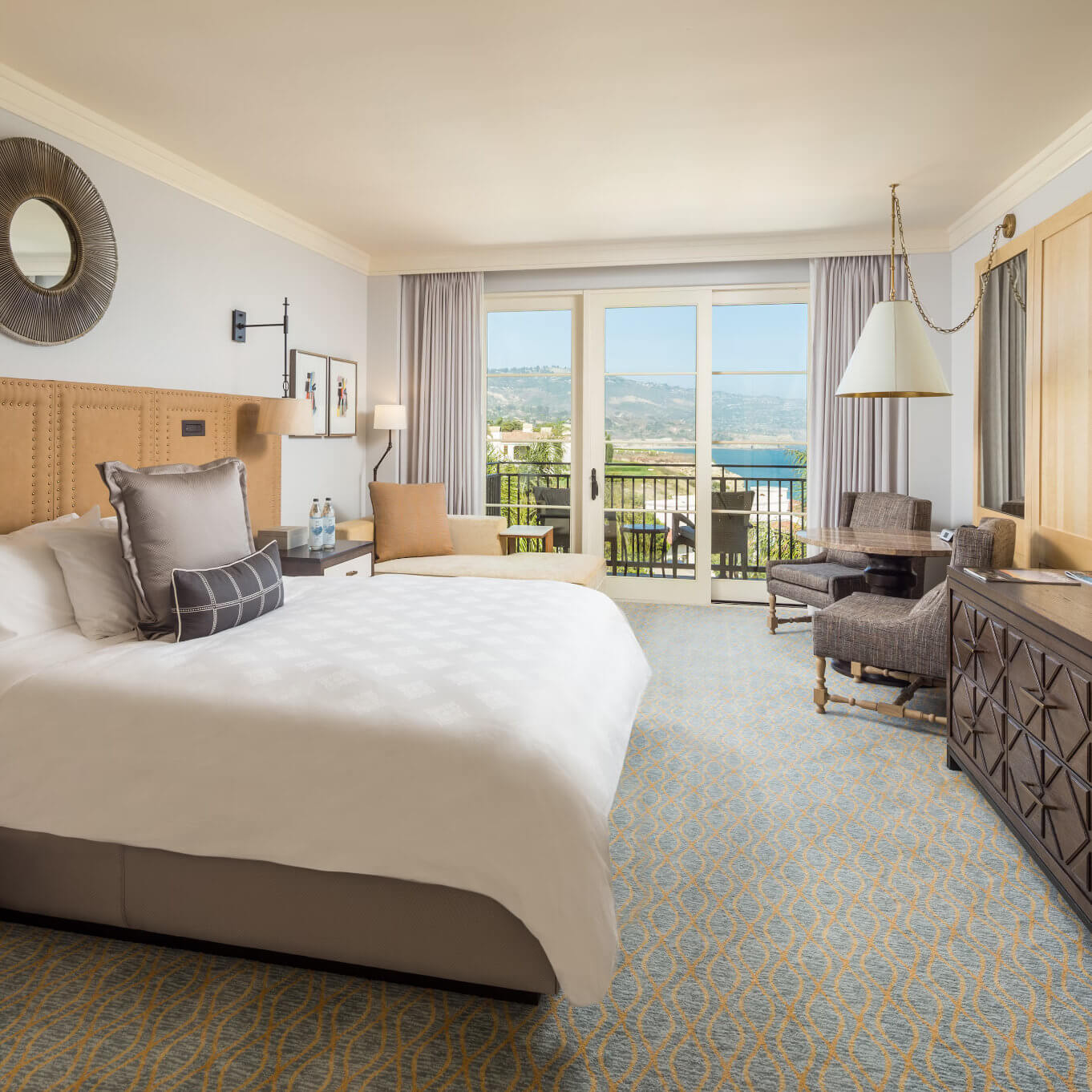 A king guest room at Terranea Resort with a large bed, patterned carpet, and a balcony with ocean views
