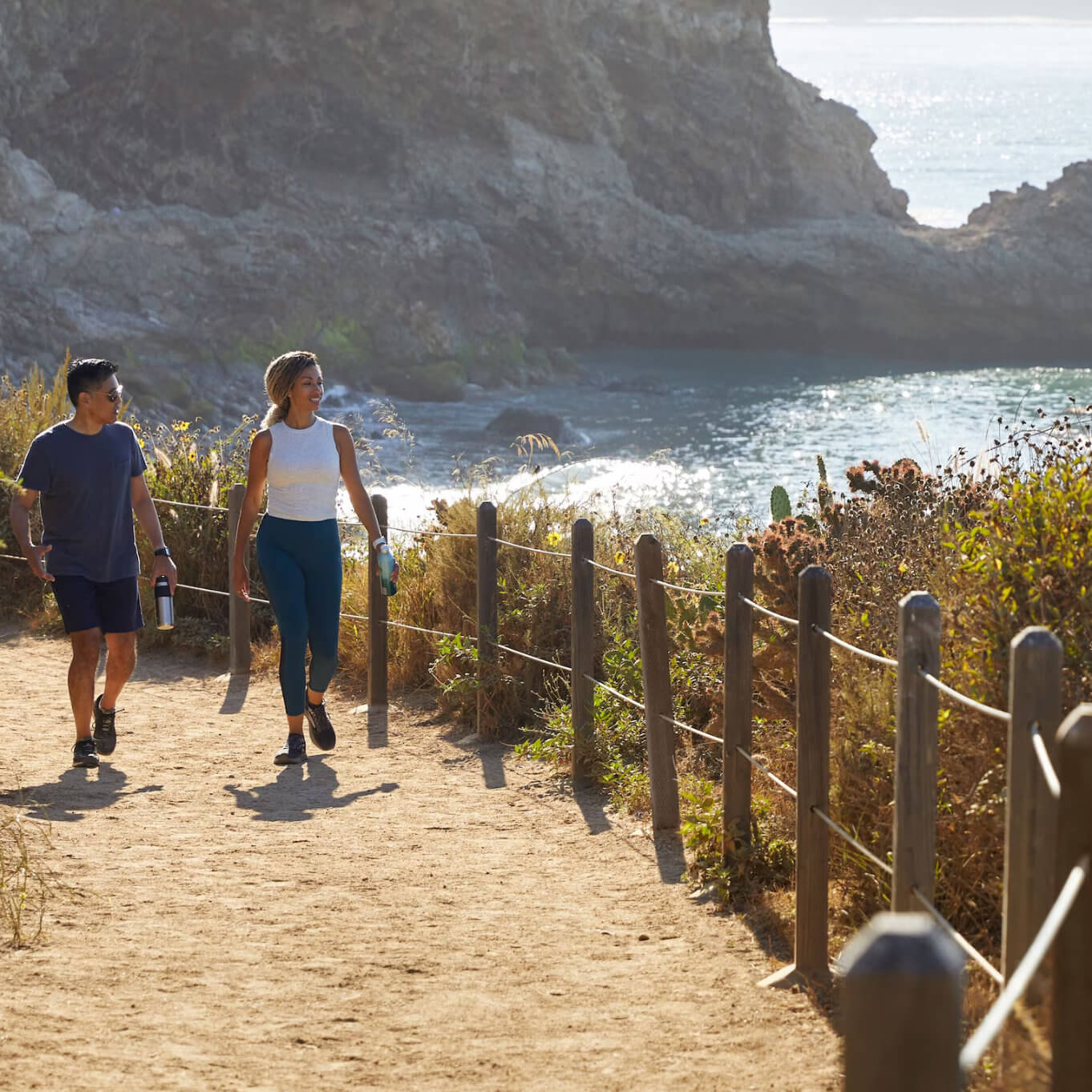 Two people walking along a coastal trail at Terranea Resort with rocky cliffs and the ocean below